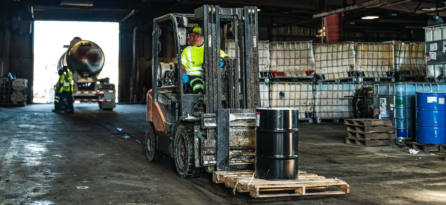 worker driving a forklift carrying an oil barrel